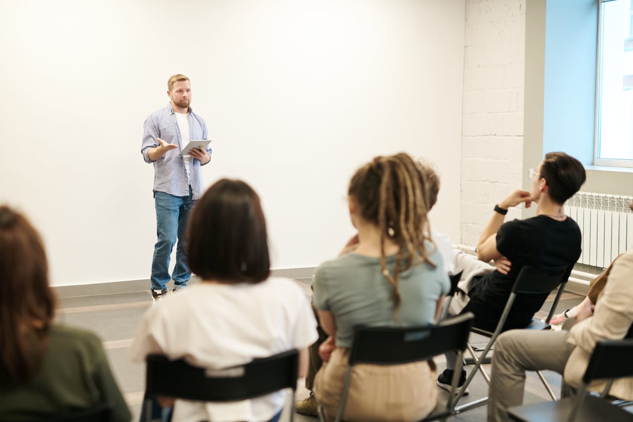about-03 Man presenting with tablet to a small seated audience in a modern indoor setting.